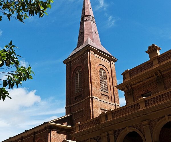 The brick tower and copper spire of St James' Church, King Street, Sydney, seen from below against a blue sky