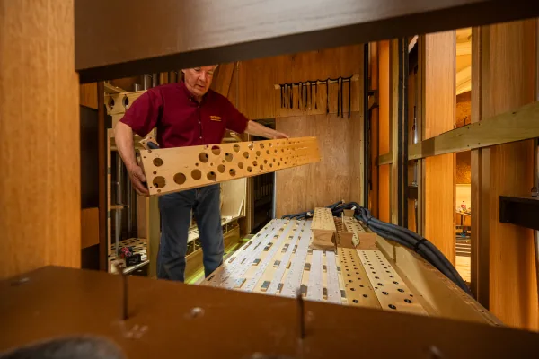 An organ builder lifting a perforated timber windchest component into place inside the Bicentennial Pipe Organ