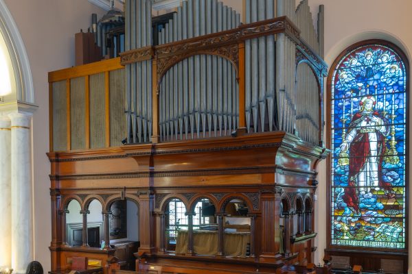 The previous pipe organ at St James' Church beside a stained glass window depicting a robed figure